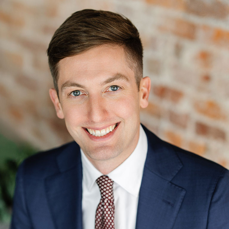 A headshot of Andy Nielsen, who wears a blue suit with a white dress shirt and tie.