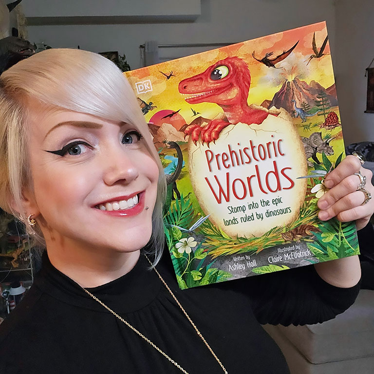 A headshot of Ashley Hall, who poses with her children's book, "Prehistoric Worlds."