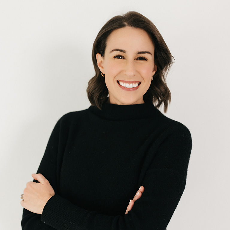 A headshot of Bailey Daar, who wears a black sweater and poses against a white background.