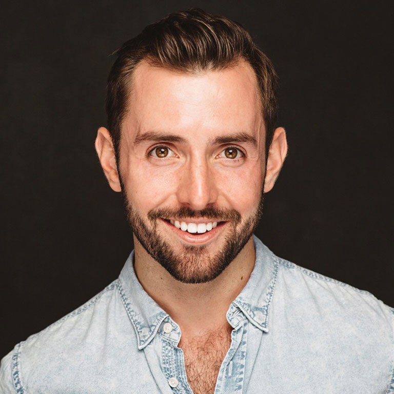 A headshot of Evan Mayer, who wears a jean button-up shirt and poses against a black background.