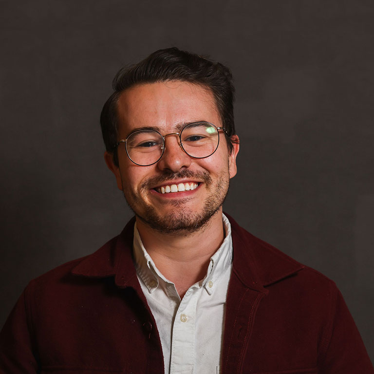 A headshot of Parker Henry, who wears a blue blazer, white dress shirt, and glasses.