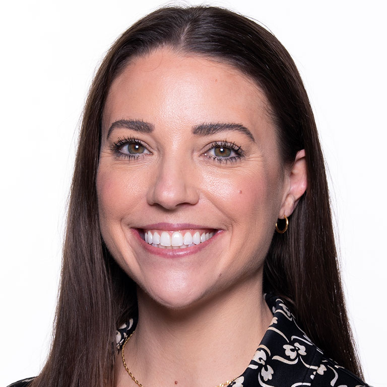 A headshot of Katie Pyfer, who wears a black and white shirt and gold circular earrings.