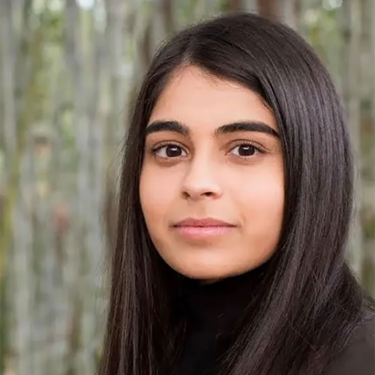 A headshot of Sneha Dave, who wears a black sweater and poses outside.