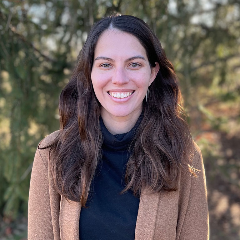 A headshot of Sofia Casasa, who wears a black shirt, brown blazer, and poses outside.