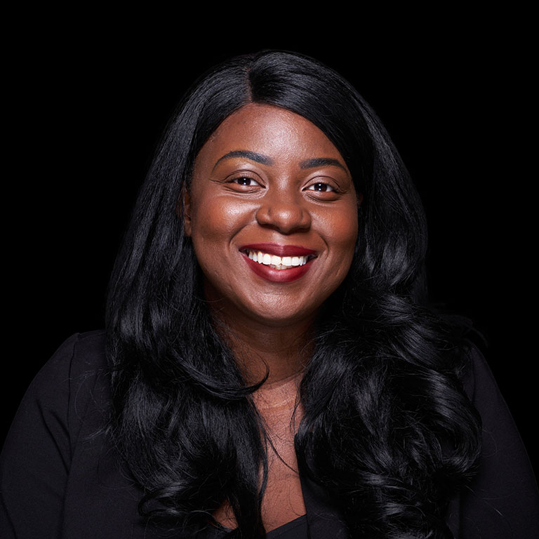 A headshot of Yalie Saweda Kamara, who wears a black blazer and poses against a black background.